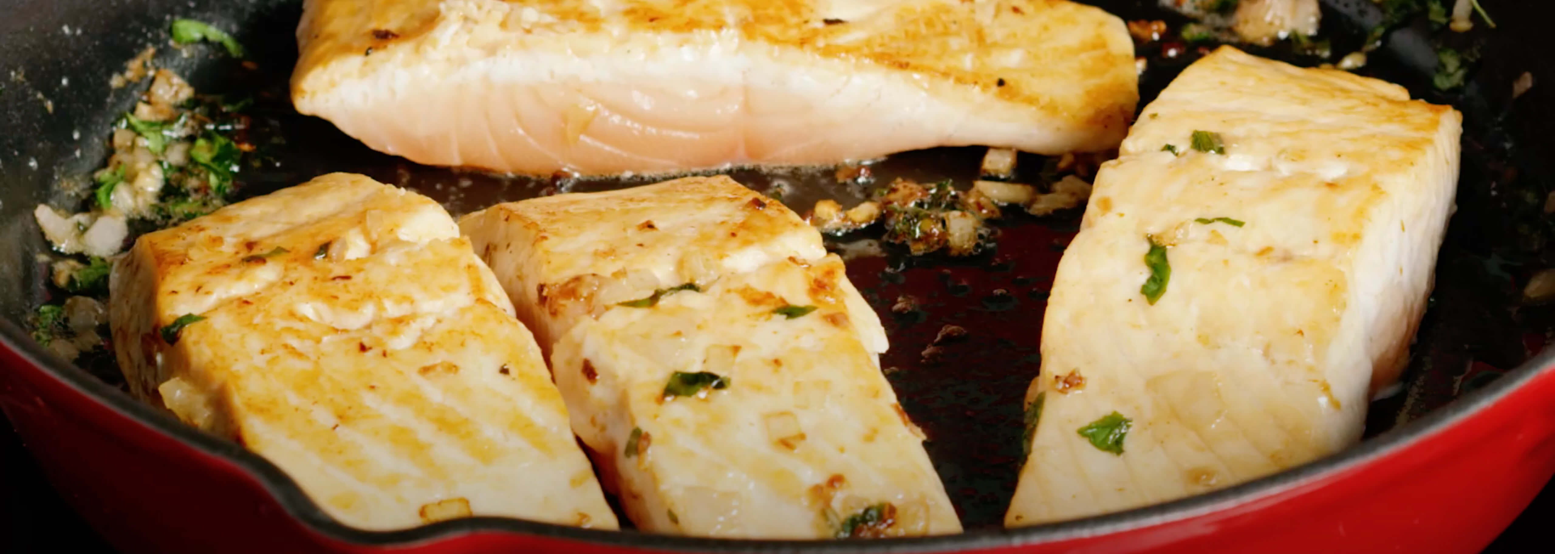 Cooked salmon in red skillet with herbs and garlic